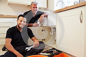 Portrait of plumber with apprentice in domestic kitchen