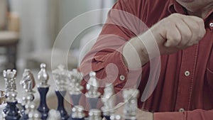 Portrait of plump man in red shirt thinking hard before to make a move with chess piece. Caucasian old man playing chess