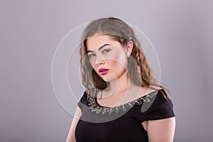 Portrait of a plus size female model posing in black dress over grey background.