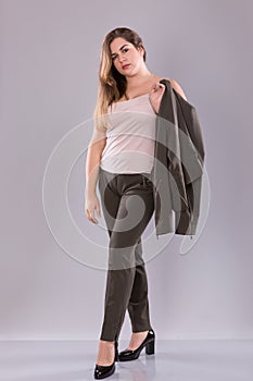 Portrait of a plus size female model posing in broun suit over grey background.