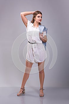 Portrait of a plus size female model posing in white dress over grey background.