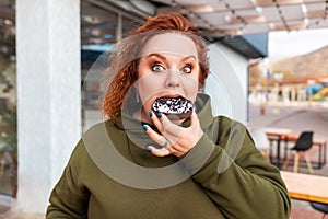 Portrait of plus sized amazement woman eating a chocolate donut. The concept of diet and nutrition