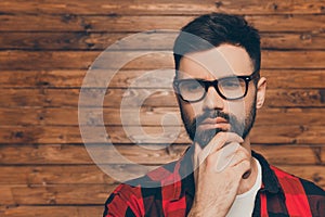 Portrait of ponder young man in glasses on backgroung of wooden wall