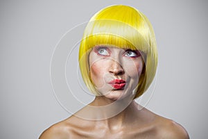 Portrait of pondering cute young woman with freckles, red makeup and yellow wig looking away and thinking about something