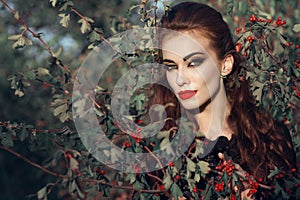 Portrait of posh redheaded woman with provocative make up standing in the berry bush and looking straight with predatory gaze