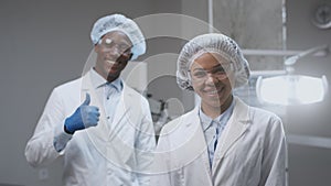 Portrait of positive african american man and woman dentists smiling to camera, male doctor gesturing thumb up