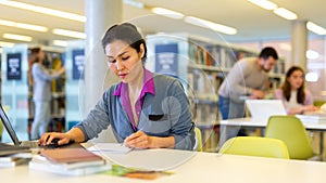 Portrait of positive asian woman with laptop in library