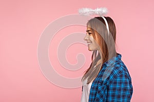 Portrait of positive beautiful angelic girl with nimbus over head smiling joyfully and looking at copy space