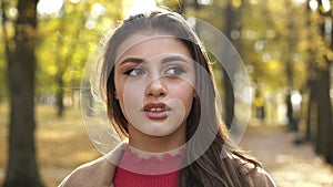 Portrait of positive brunette with make-up looks at camera in sunny autumn park