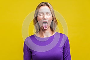 Portrait of positive carefree woman demonstrating tongue. indoor studio shot isolated on yellow background