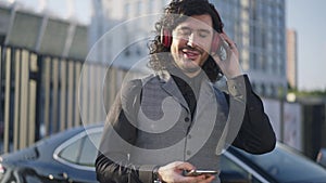 Portrait of positive Caucasian man turning on playlist on smartphone listening to music in headphones smiling. Happy