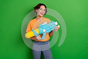 Portrait of positive charming girl toothy smile hands hold water pistol isolated on green color background