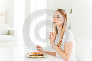 Portrait of positive cheerful lady feel satisfied delight have dinner with proteins vitamins lick fork knife sit chair