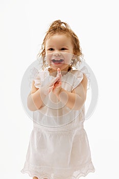 Portrait of of positive, cheerful little toddler, laughing and clapping of joy and happiness baby girl in cute dress