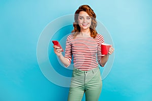 Portrait of positive cheerful woman hold cup with latte use smartphone texting typing social network notification wear