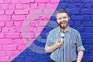 Portrait of positive cheerful young stylish man with mustache and beard and glasses in hands posing against blue-violet