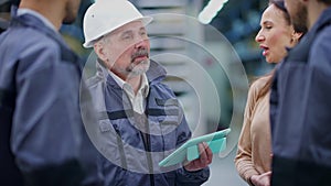 Portrait of positive confident experienced professional foreman in hard hat instructing employees in warehouse. Senior