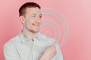 Portrait of positive curious man indicate finger empty space look side away on pink background