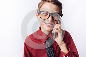 Portrait of positive and emotional schoolboy talking on phone, white background, glasses, red shirt, business theme, advertising,