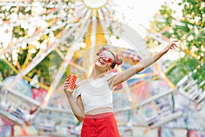 Portrait of a positive funky girl holding a glass with a drink or smoothie in red funny glasses