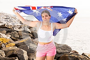 Portrait of a positive girl with the flag of Australia on the seashore on sunny day