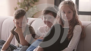 Portrait of positive girl and two boys sitting on the couch looking at the camera smiling. Siblings relationship