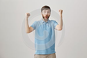 Portrait of positive good-looking slim european bearded man, standing over gray background with raised fists and excited