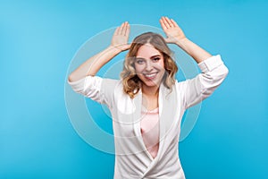 Portrait of positive good-natured woman making bunny ears gesture and smiling. isolated on blue background