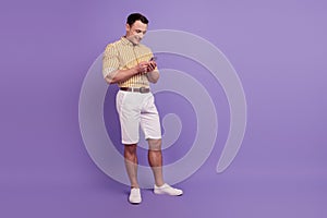 Portrait of positive handsome guy texting chatting cellphone on violet background