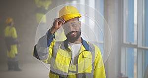 Portrait of positive, handsome young African-American builder in hardhat smiling at camera