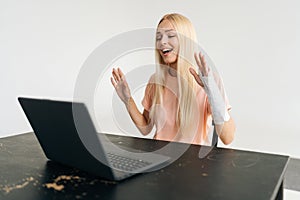 Portrait of positive injured blonde young woman with broken arm wrapped in plaster bandage having video call or online