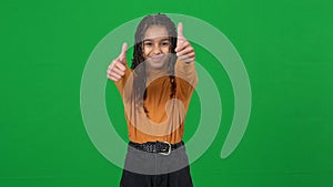 Portrait of positive joyful teen African American girl showing thumbs up looking at camera on green screen. Happy