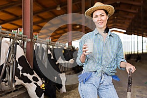 Portrait of a positive kazakh farmer woman in a cowshed, holding a glass of milk