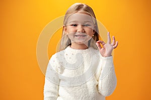 Portrait of positive kid girl show okay sign over yellow background