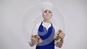 Portrait of positive little cook breaking crunchy bread smelling delicious pastry smiling looking at camera. Front view