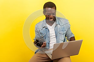 Portrait of positive male photographer holding digital dslr camera and laptop. studio shot isolated on yellow background