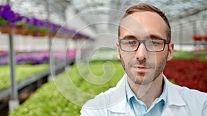Portrait of positive man agriculture engineer in glasses and uniform posing at greenhouse
