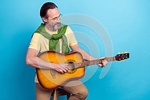 Portrait of positive man sitting chair playing acoustic guitar sing isolated on blue color background