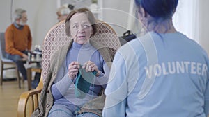 Portrait of positive mature Caucasian woman talking with unrecognizable volunteer in nursing home. Senior retiree