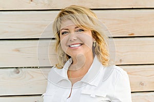 Portrait positive mature middle-aged woman smiling close-up. Blonde woman, outdoor wooden background