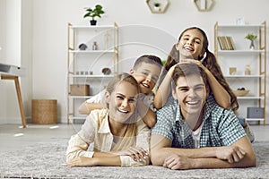 Portrait of positive mother, father, son and daughter lying together on rug in living room.