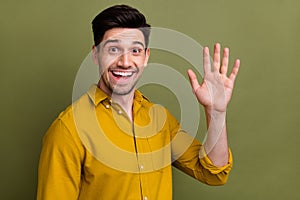 Portrait of positive nice young man beaming smile arm palm waving hi isolated on khaki color background