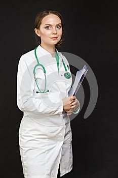 Portrait of Positive Professional Female GP Doctor Posing in Doctor`s Smock and Endoscope Against Black