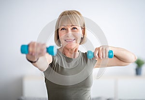 Portrait of positive senior lady exercising with dumbbells at home during covid-19 quarantine