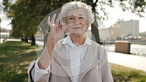 Portrait of positive senior woman showing ok hand gesture and smiling outdoors in urban street