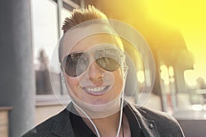 Portrait of a positive smiling young businessman of European appearance in sunglasses and headphones listening to music on the