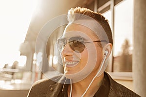 Portrait of a positive smiling young businessman of European appearance in sunglasses and headphones listening to music on the