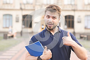 Portrait of a positive student standing with books in his hands against the background of the building and smiling photo