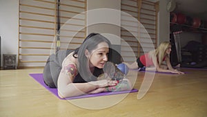 Portrait of positive tattooed brunette woman lying on yoga mat and smiling. Beautiful adult Caucasian sportswoman