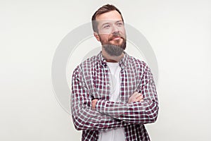 Portrait of positive thoughtful bearded man standing with crossed hands, looking aside with dreamy happy face. white background